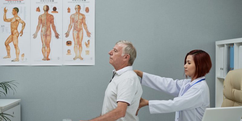 Physiothrapist checking spine of senior man in her office