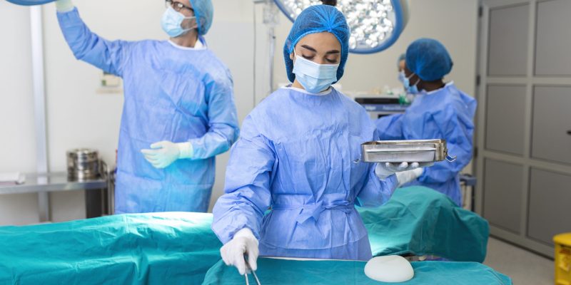 Female surgeon in surgical uniform taking surgical instruments at operating room. Young woman doctor in hospital operation theater